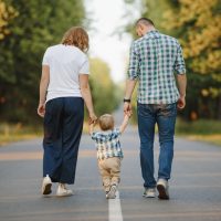 Parents holding their little son are walking a road